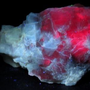 May include: A close-up of a mineral specimen with a striking contrast of colors. The top right section glows a vibrant red, while the rest of the rock displays a mix of white and light blue hues. The background is black.
