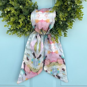 K&ouml;nnte beinhalten: Ein Kranz mit gr&uuml;nen Bl&auml;ttern und einer Schleife aus Stoff mit Blumenmuster. Die Schleife ist zu einem Knoten gebunden und die Enden h&auml;ngen herunter.