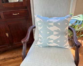 May include: A traditional armchair with a light blue and white striped fabric. A square pillow with a light blue and white abstract pattern rests on the chair. The chair has dark wood arms and legs, and is placed near a window.