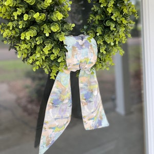 May include: A green wreath with a light blue, green, and beige patterned bow. The bow is tied in a knot and hangs down from the wreath.