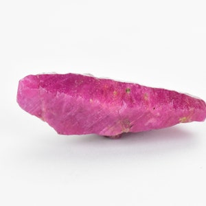 May include: A large, rough, pink ruby gemstone with a pointed end. The ruby has a natural, unpolished finish.