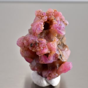 May include: A cluster of pink ruby crystals, some with a rough, natural texture, others with smooth, polished surfaces. The crystals are arranged in a cluster, creating a unique and eye-catching display.