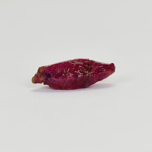 May include: A deep red ruby crystal with a pointed tip and a rough, natural surface.