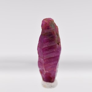 May include: A deep pink ruby crystal with a pointed tip and striations on its surface.