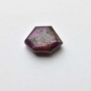 May include: A faceted purple gemstone with gold inclusions. The gemstone is cut in a hexagonal shape.