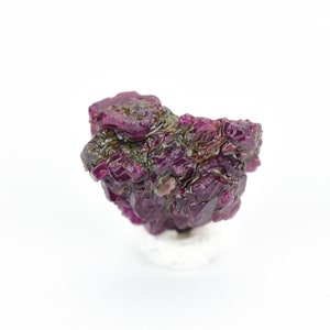 Puede incluir: Un cúmulo de cristales de rubí de color púrpura intenso con una superficie rugosa y texturizada. Los cristales están dispuestos en un patrón aleatorio y orgánico, creando una exhibición única y llamativa.