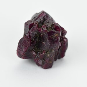 May include: A deep red ruby crystal with a rough, faceted surface. The crystal is a cluster of smaller crystals that have grown together.