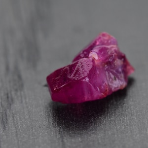 May include: A deep pink ruby crystal with multiple facets. The crystal is rough and has a natural, unpolished look.