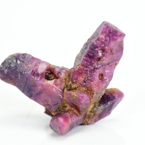 May include: A cluster of pink ruby crystals with a rough, natural appearance. The crystals are intergrown and have a deep, rich pink color.