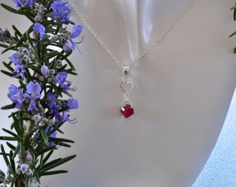 May include: A silver necklace with a heart charm and a red gemstone pendant.