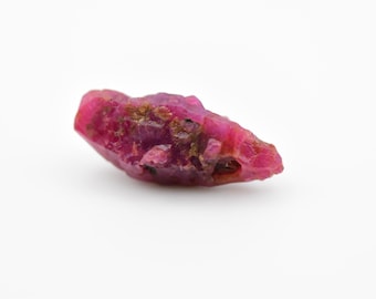 May include: A raw, pink ruby gemstone with a rough, irregular shape. The ruby has a deep, rich color and is a natural, unpolished stone.