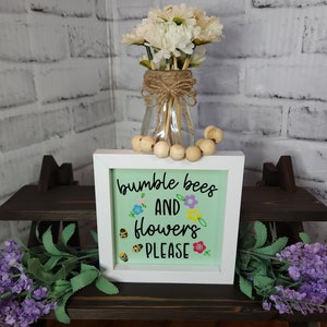 May include: A white framed sign with a green background and the text "bumble bees and flowers please" in black script. The sign is decorated with small yellow bees and colorful flowers.