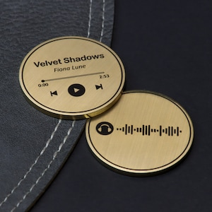 May include: Two gold-coloured metal discs. The top disc has a music player interface with the text "Velvet Shadows" and "Fiona Lune" and the time "0:00" and "2:53". The bottom disc has a headphone icon and a barcode.