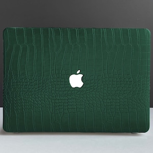Puede incluir: Una funda para portátil verde con un patrón de piel de cocodrilo. La funda tiene un logotipo de Apple blanco en la parte delantera.