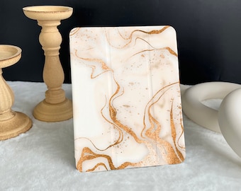 May include: A white and gold marble-patterned iPad case with a gold glitter finish.