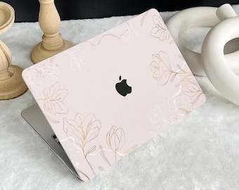 May include: A pink laptop skin with a floral design. The design features white and gold outlines of flowers and leaves on a light pink background. The Apple logo is visible on the laptop.