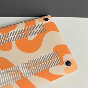May include: A laptop case with a white and orange abstract pattern. The case has a vent on the back and two black rubber feet.