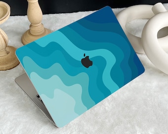 May include: A laptop with a blue and teal wave pattern cover. The cover features a black Apple logo. The laptop is open, revealing the keyboard and screen. The design has a gradient effect, with darker shades at the top and lighter shades at the bottom.