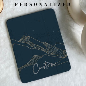 May include: A dark blue tablet case with a gold outline of mountains and stars. The text "Custom" is written in white cursive on the case.
