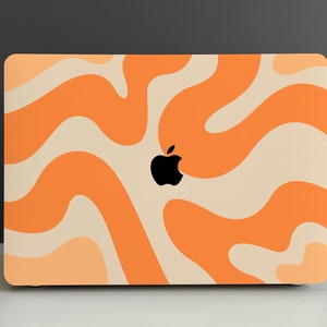 May include: A laptop computer with a cream and orange abstract swirl pattern on the cover. The Apple logo is visible in the centre of the cover.