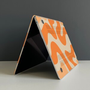 May include: A laptop computer with a white and orange abstract pattern on the back. The laptop is closed and sitting on a white surface.
