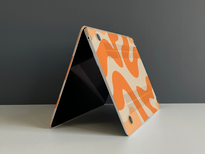 May include: A laptop computer with a white and orange abstract pattern on the back. The laptop is closed and sitting on a white surface.