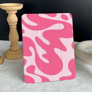 Puede incluir: Funda para iPad con patrón abstracto rosa y blanco. La funda tiene un diseño moderno y abstracto con remolinos rosas y blancos.