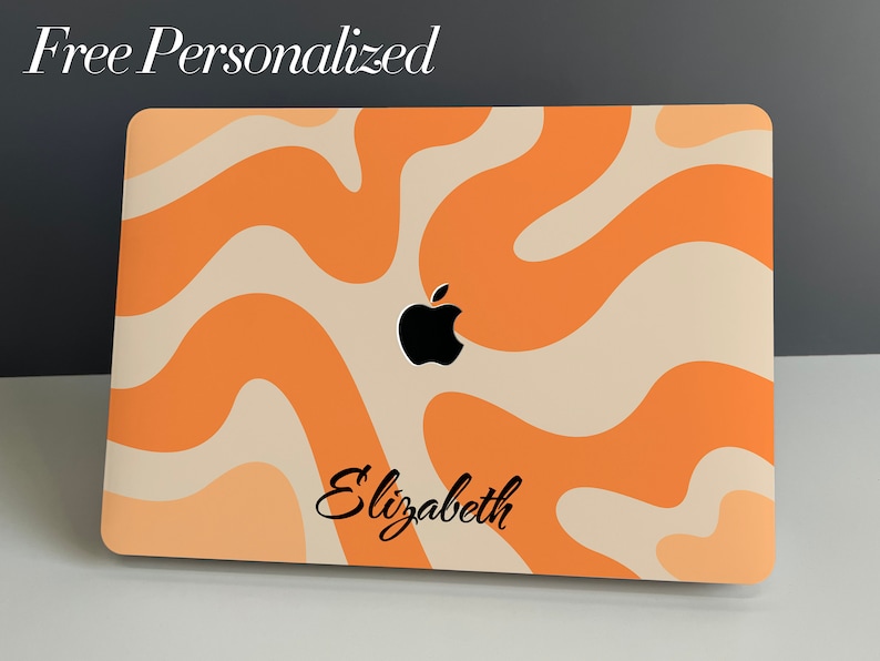 May include: A laptop computer with a personalised orange and cream abstract design. The Apple logo is visible on the lid, and the name "Elizabeth" is printed on the bottom of the laptop.
