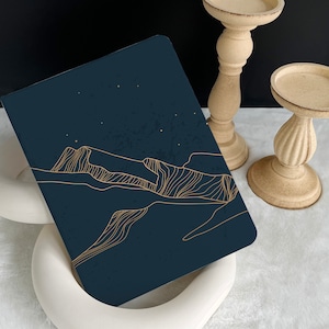 May include: A dark blue notebook with a gold line drawing of a mountain range and stars on the cover.