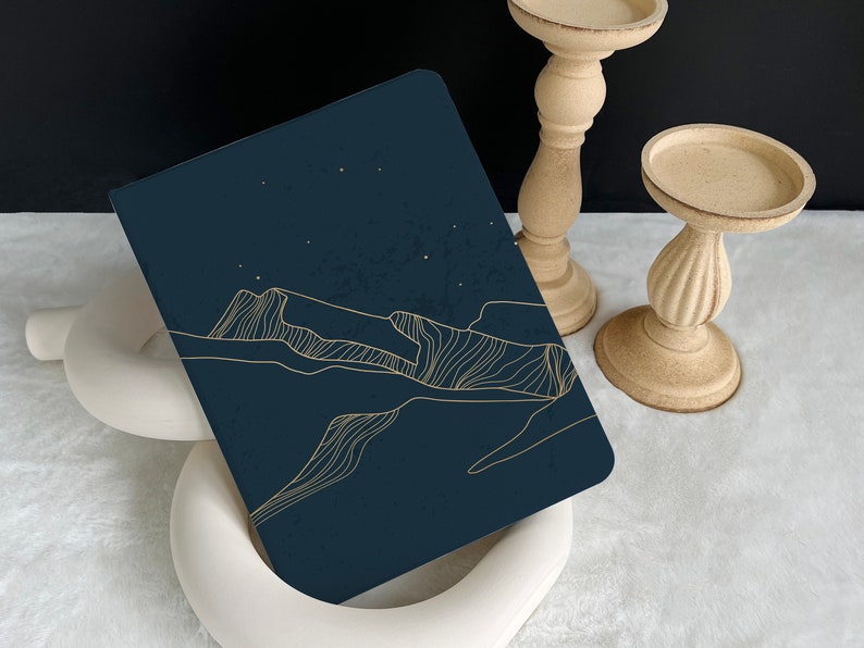 May include: A dark blue notebook with a gold line drawing of a mountain range and stars on the cover.