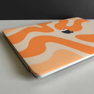 May include: A white laptop with an orange and cream abstract swirl pattern on the lid. The Apple logo is visible on the lid.