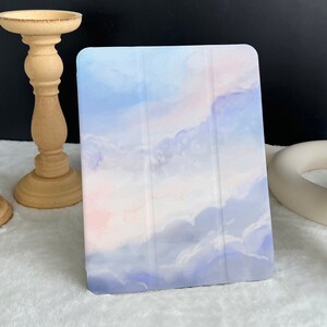 May include: A light blue, pink, and white tablet case with a watercolor cloud design.