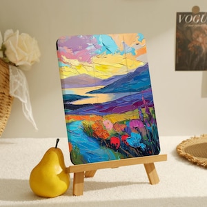 May include: A colorful landscape painting on a canvas with a wooden easel. The painting depicts a river flowing through a valley with mountains in the background. The sky is a vibrant mix of pink, orange, and yellow.
