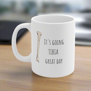 May include: White ceramic mug with a black and white illustration of a bone and the text "It's going tibia great day".