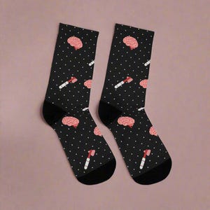 Pu&ograve; includere: Un paio di calzini neri con un motivo a pois bianchi. I calzini presentano un cervello rosa e un martello rosa.