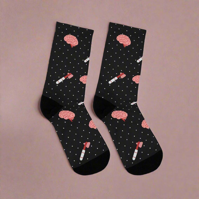Pu&ograve; includere: Un paio di calzini neri con un motivo a pois bianchi. I calzini presentano un cervello rosa e un martello rosa.