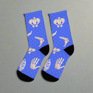 May include: A pair of blue socks with a white polka dot pattern. The socks feature a repeated design of various bones, including a pelvis, femur, and hand.