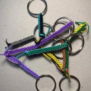 May include: A collection of colorful keychains with woven fabric straps and silver metal rings.