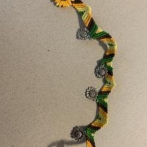 May include: A green, yellow, and black friendship bracelet with a sunflower charm at one end and five silver sunflower charms along the length of the bracelet.