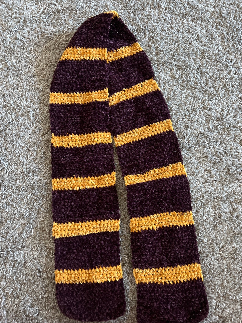 May include: A maroon and gold striped scarf made of fuzzy yarn.