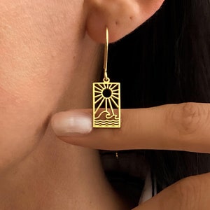 May include: Gold earrings with a sun and wave design. The earrings are in the shape of a rectangle.