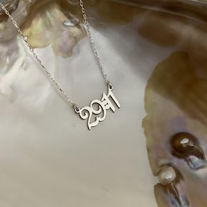 The necklace is photographed resting on a natural shell, emphasizing the reflective shine of the silver and the high-quality craftsmanship.