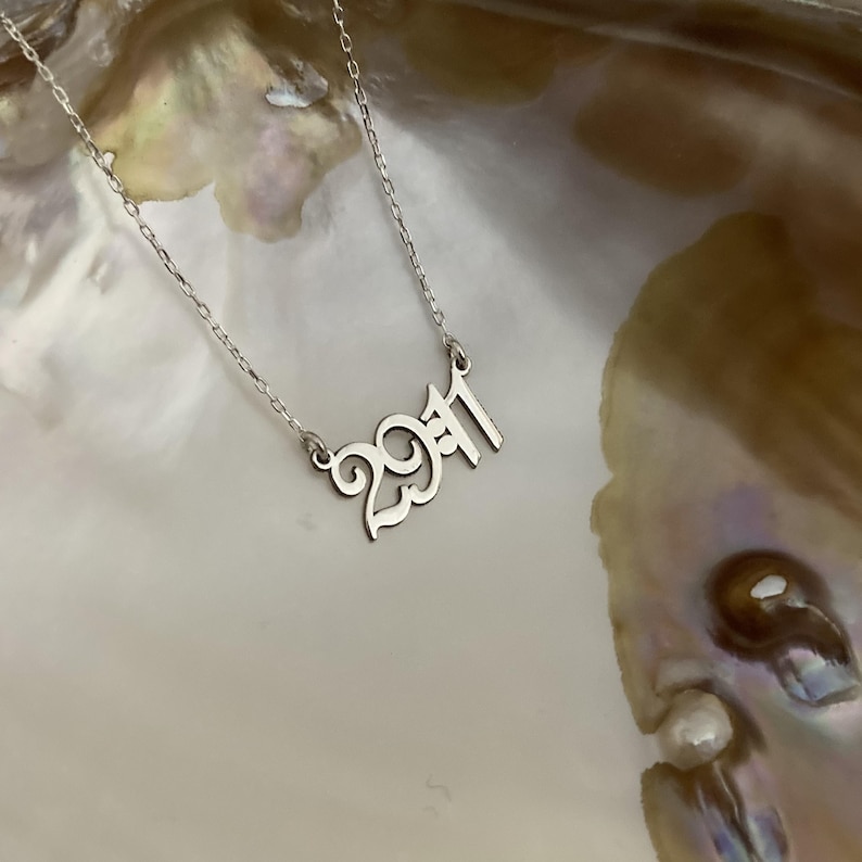 The necklace is photographed resting on a natural shell, emphasizing the reflective shine of the silver and the high-quality craftsmanship.
