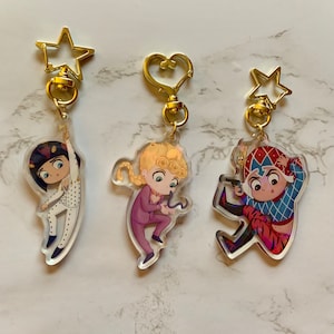 May include: Three acrylic keychains featuring cartoon characters. Each keychain has a gold-colored clasp. The characters are depicted in various poses and outfits, with vibrant colors and detailed designs. One keychain has a star-shaped clasp, another a heart-shaped clasp, and the third a star-shaped clasp.