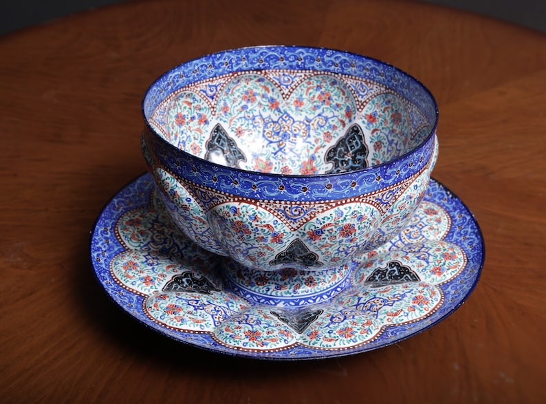 May include: A decorative bowl and saucer set with intricate floral and geometric patterns in shades of blue, white, and red. The bowl has a pedestal base and the saucer has a scalloped edge.