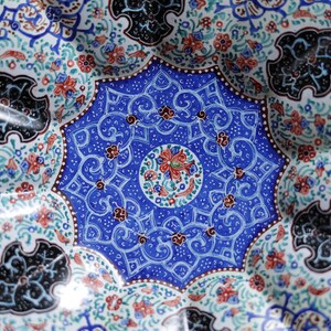 May include: A blue and white ceramic plate with intricate floral and geometric designs. The center of the plate features a circular design with red, green, and blue accents.