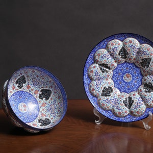 May include: Two decorative plates with intricate blue, white, and red floral patterns. The larger plate is on a stand and the smaller plate is lying on its side.