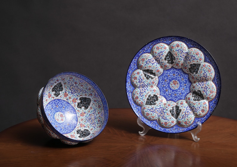 May include: Two decorative plates with intricate blue, white, and red floral patterns. The larger plate is on a stand and the smaller plate is lying on its side.