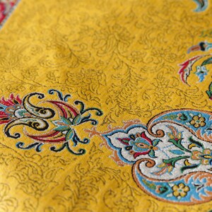May include: A yellow fabric with a paisley pattern in shades of blue, red, and green. The fabric has a subtle sheen and a textured surface.