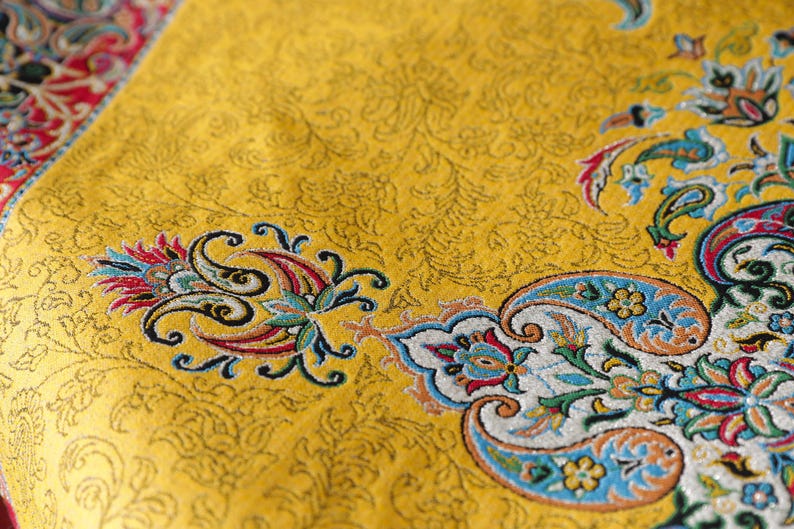 May include: A yellow fabric with a paisley pattern in shades of blue, red, and green. The fabric has a subtle sheen and a textured surface.